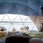 Interior of geodesic dome with view of coffee table, chairs, window and wood stove