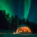 white geodesic dome in the forest in winter with a view of the northern lights