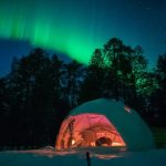 white geodesic dome in the forest in winter with a view of the northern lights