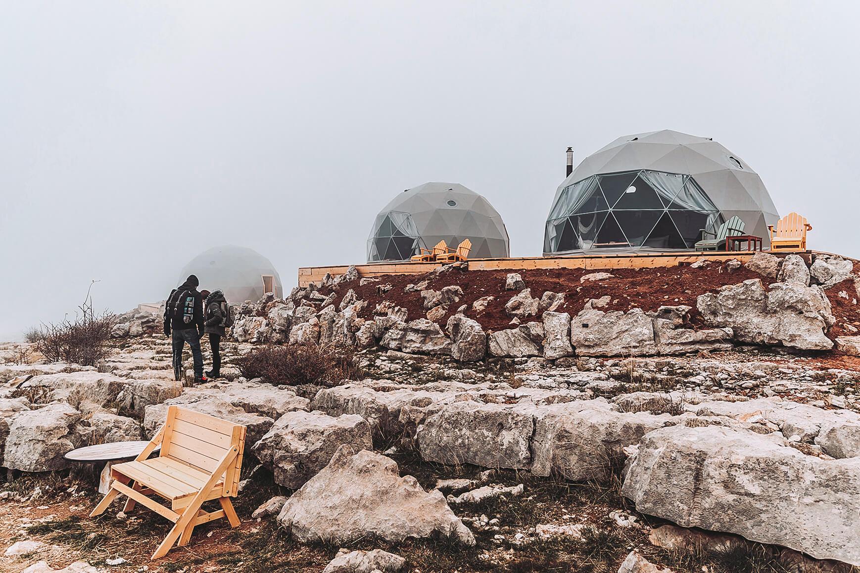 a woman and a man against a background of white geodesic domes located on rocks