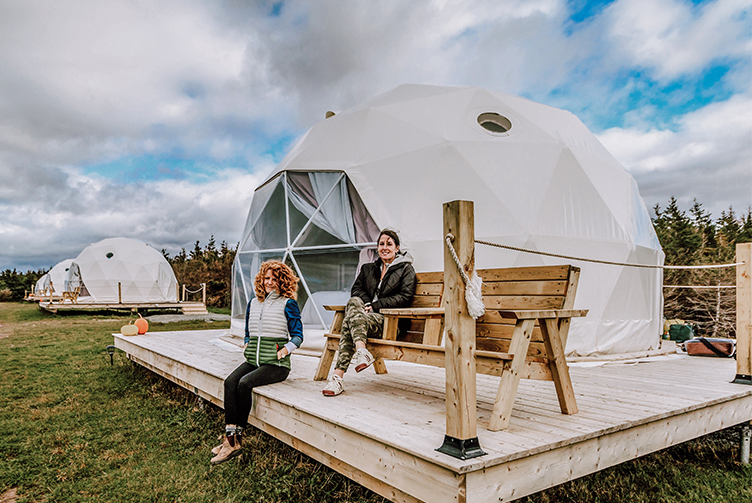 women sitting in front of white glamping geodesic dome