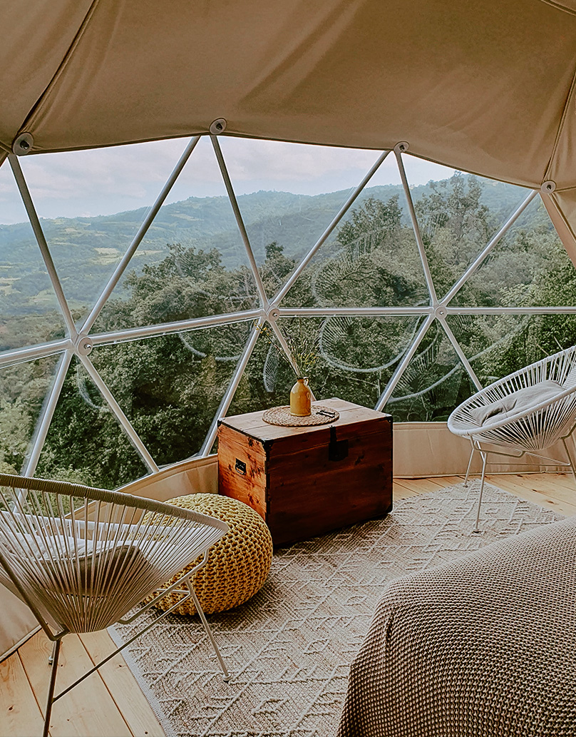 interior of geodesic dome with view at bed, table, chairs, window and insulation, in the background landscape