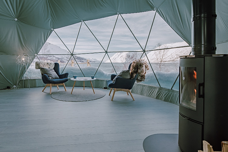 interior of geodesic dome with view at window, coffee table, chairs, fireplace and insulation, in the background winter