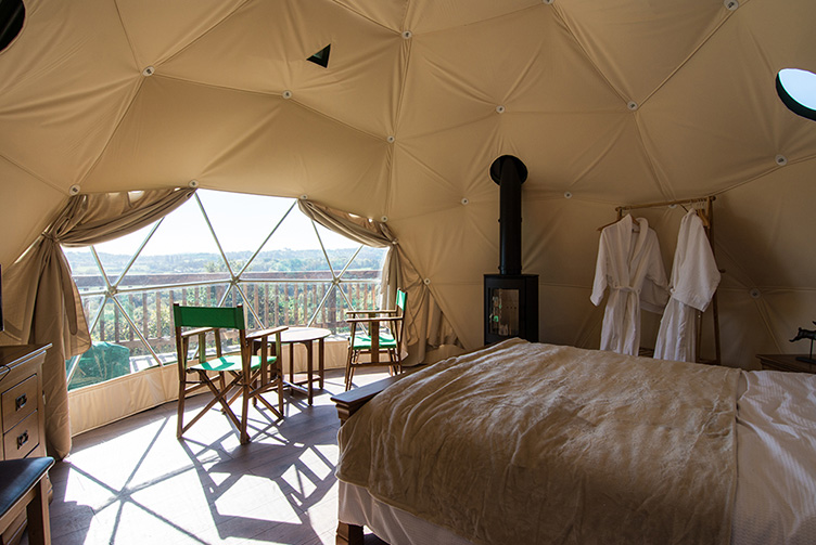 inside of geodesic dome with a bed, a stove and chairs and a table
