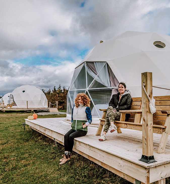 two women in front of a white geodesic dome, with white geodesic domes