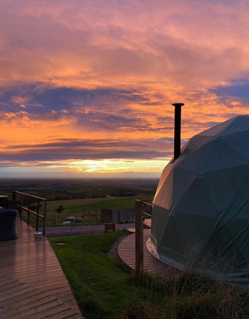 green geodesic dome on wooden platform with view at sunset