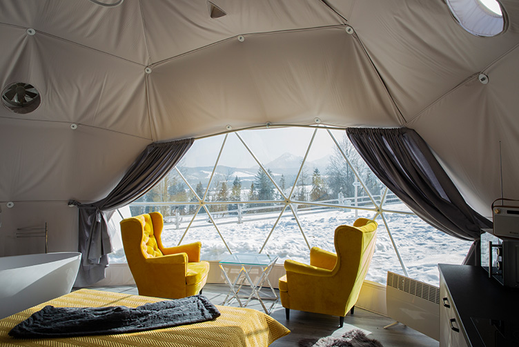 interior of a geodesic dome with a view of armchairs, a coffee table and a window, winter weather outside the window