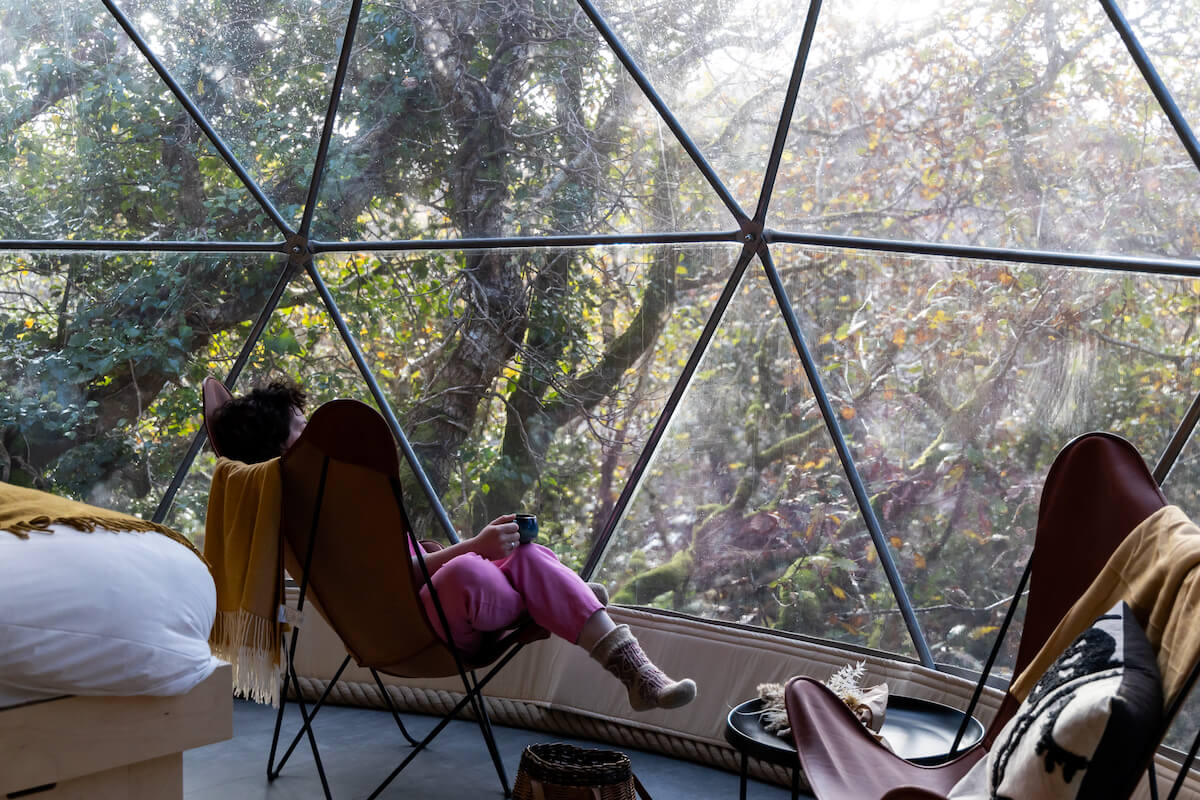 woman sitting on chair in front of window inside of geodesic dome