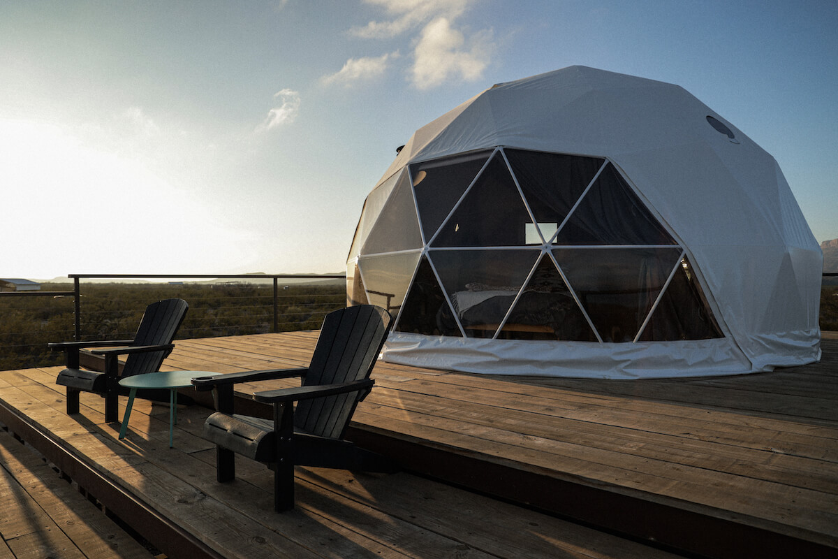 two armchairs and a table in front of white geodesic dome on wooden deck