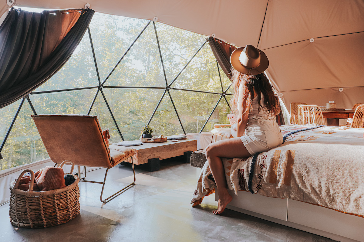 woman sitting on a bed inside of geodesic dome with a window and a chair