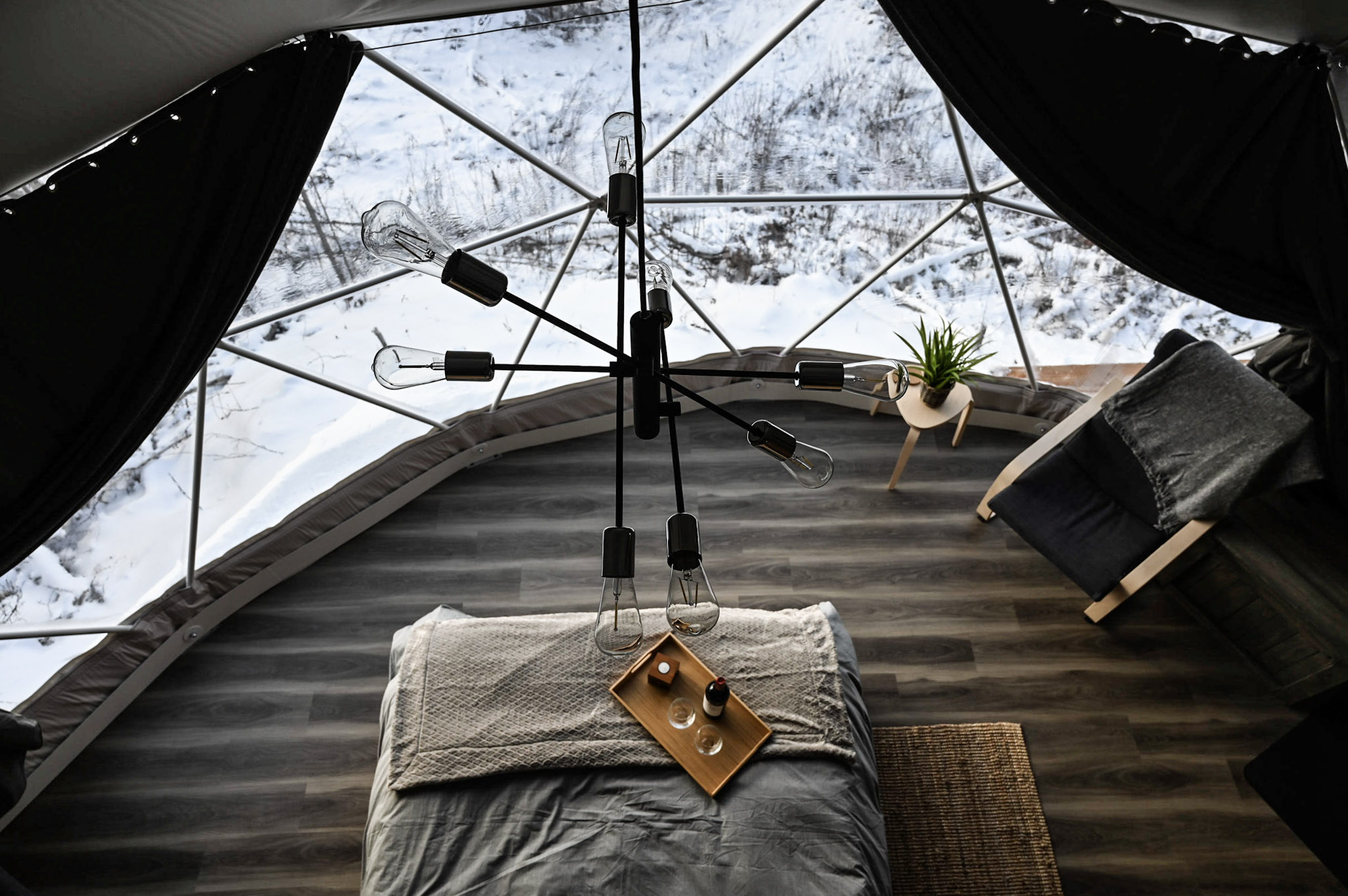 inside of geodesic dome with a bed, an armchair, a lamp and a window