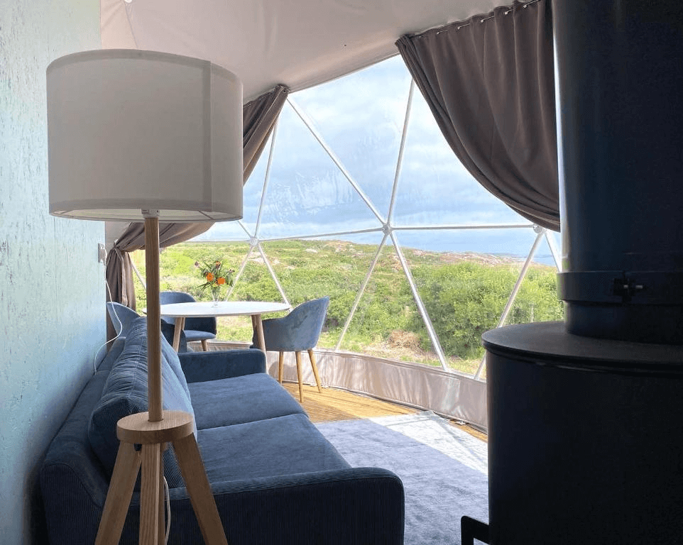 inside of geodesic dome with a blue sofa, a stove, a lamp and a window