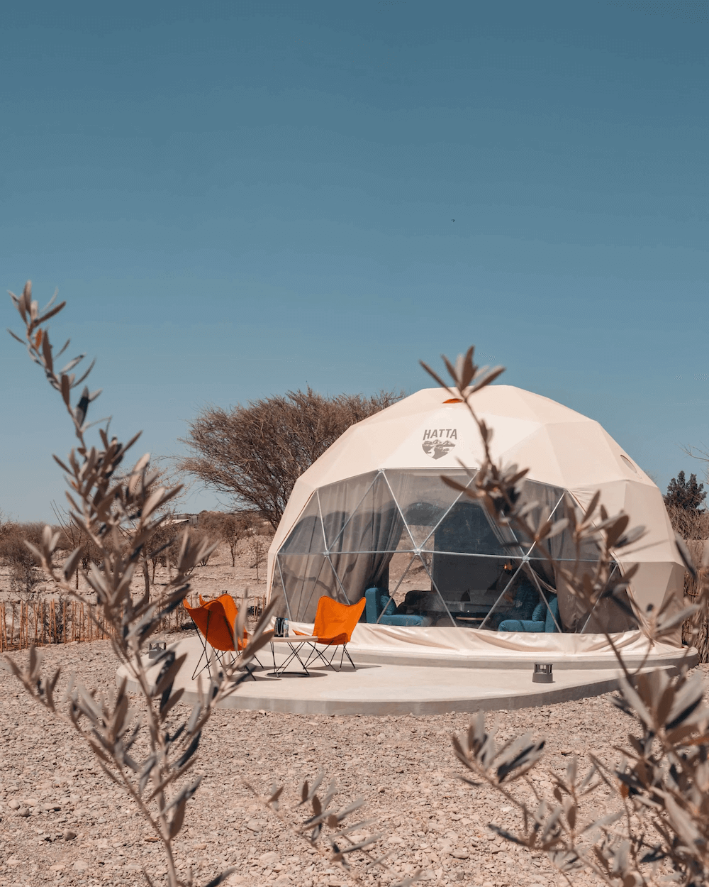 three orange chairs in front of white geodesic dome with logo Hatta on the desert
