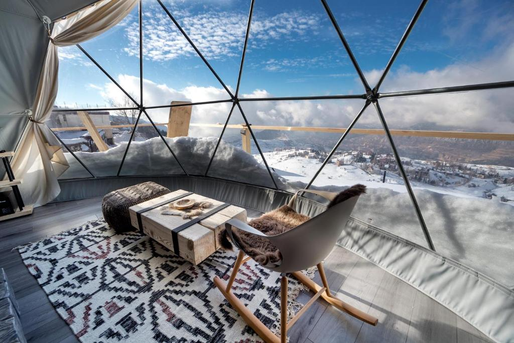 inside of geodesic dome with a chair, a table and a window with a view at snowy field