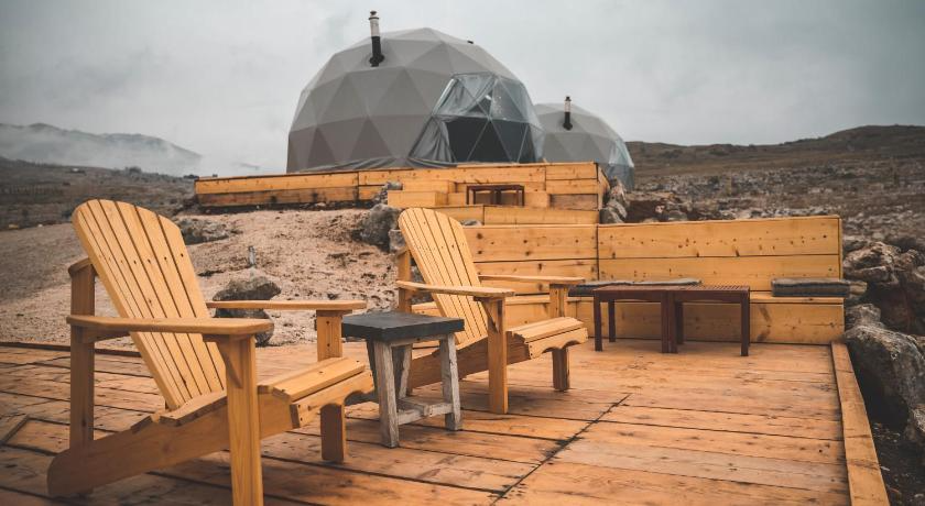 two grey geodesic domes on wooden deck with two armchairs and two tables on terrace