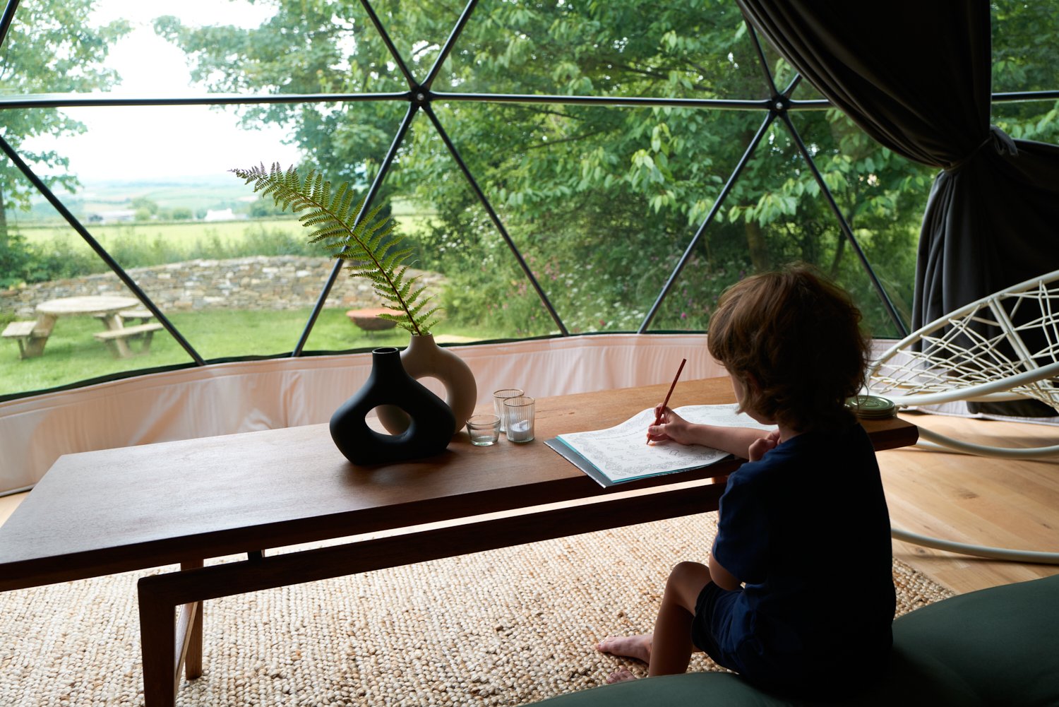 a kid sitting in front of table and a window inside of geodesic dome