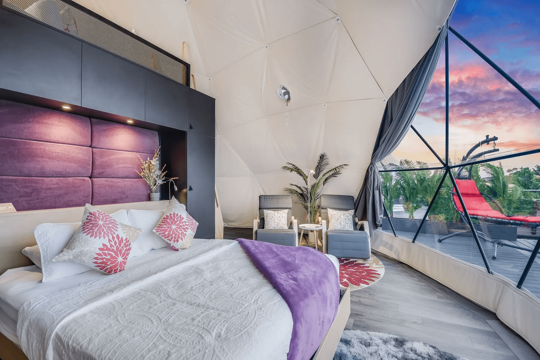 inside of geodesic dome with a bed, two armchairs, a carpet and a window