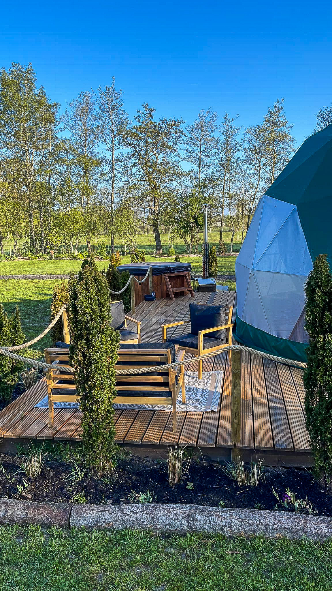 green geodesic dome on wooden deck with a tree and a table with two chairs