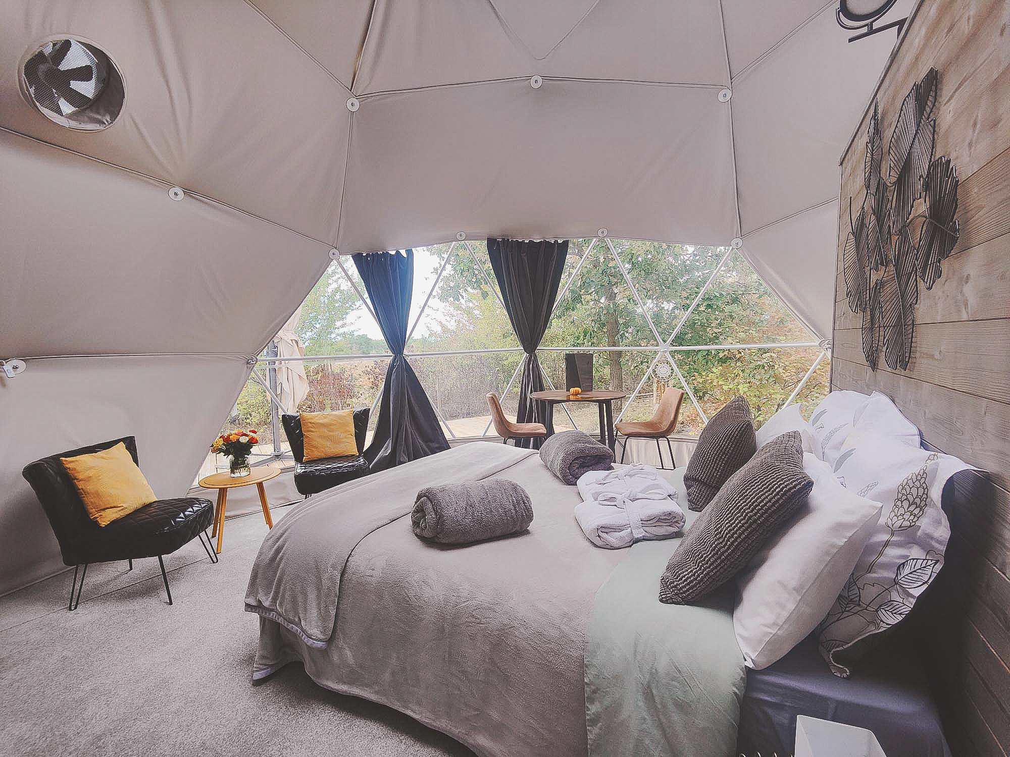 inside of geodesic dome with four armchairs, a bed and view through window