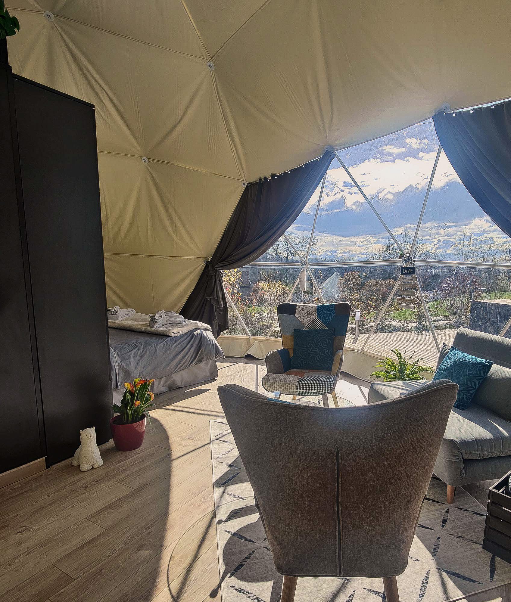 inside of geodesic dome with three armchairs, a bed and view through window