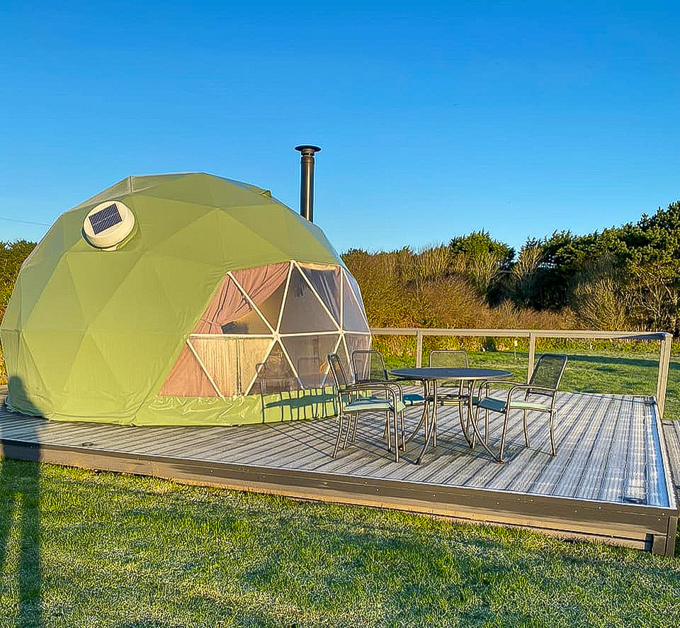 green geodesic dome on wooden deck with some chairs and a table