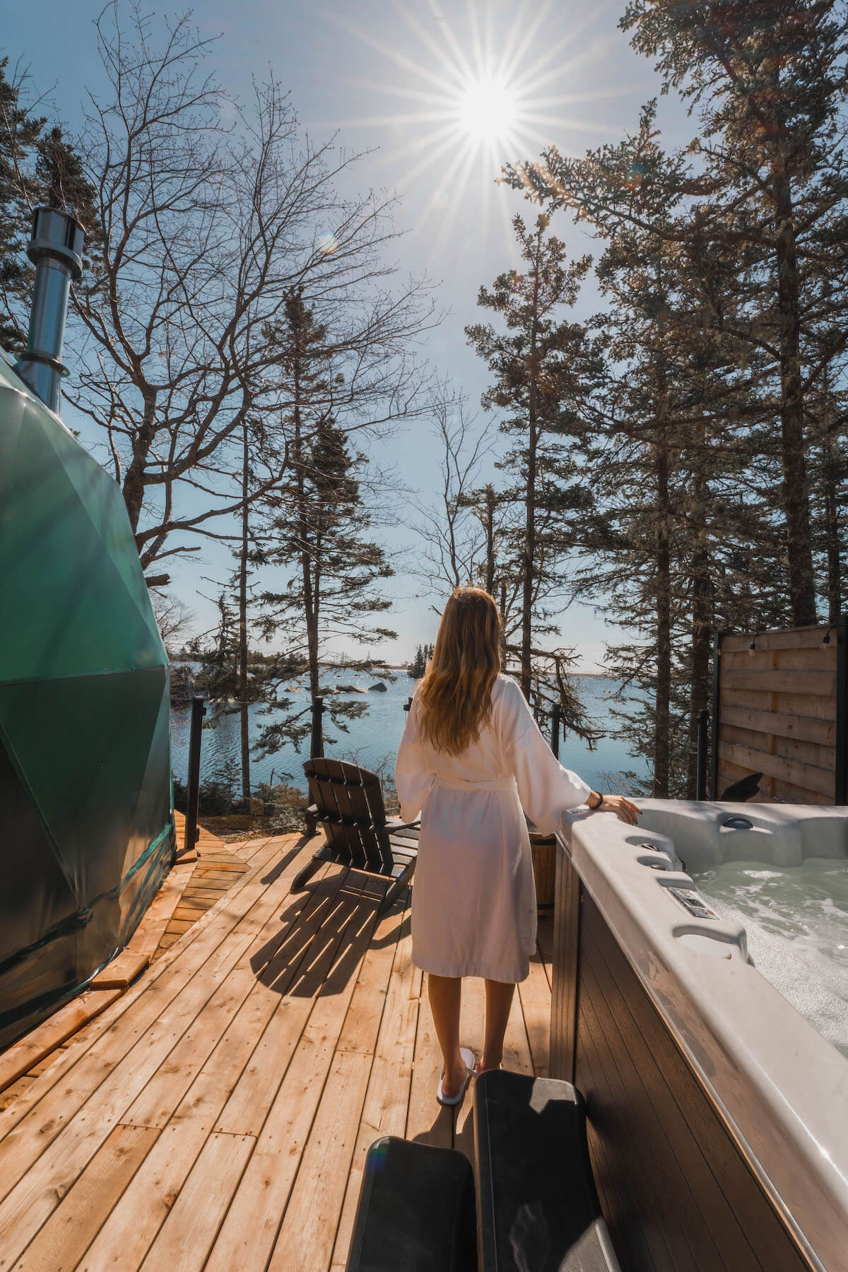 a woman standing near jacuzzi near green geodesic dome with a view on a lake