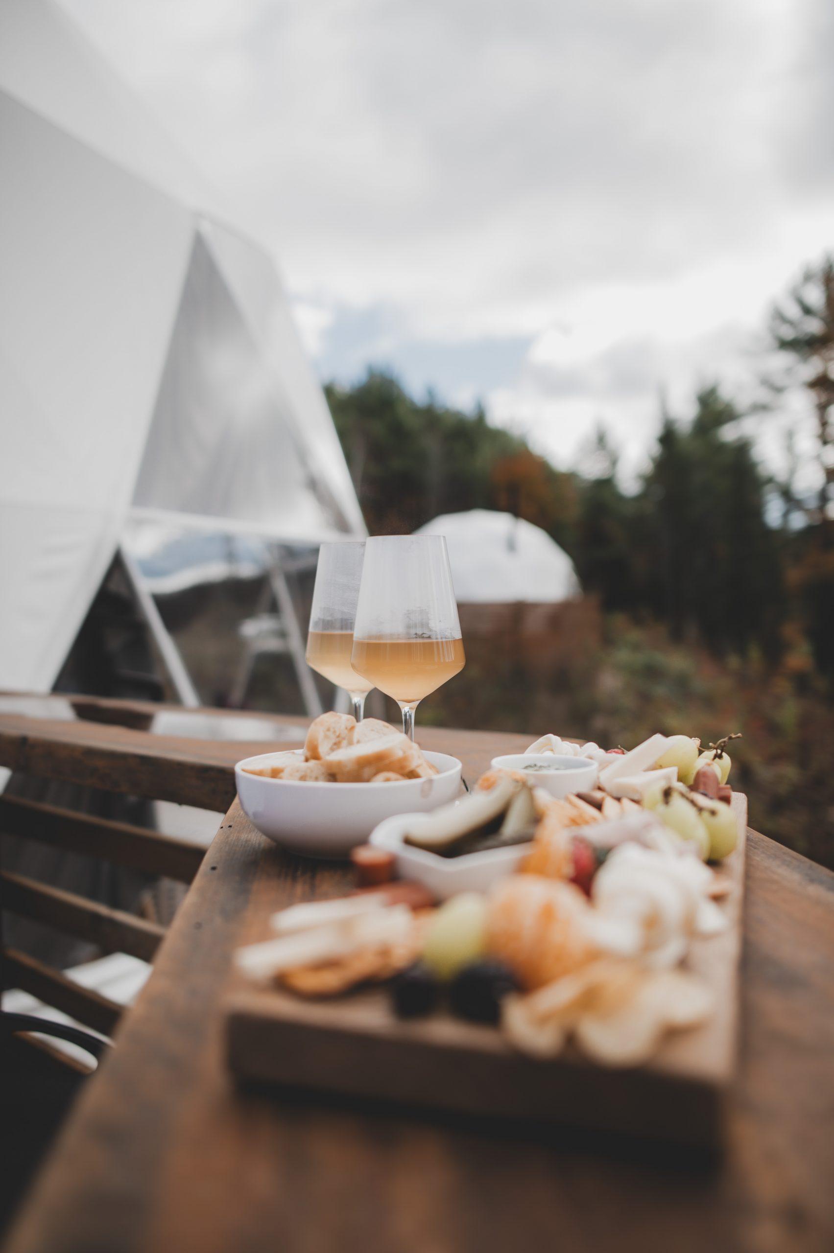 food and glasses of wine on a wooden board, with a geodesic dome in the background