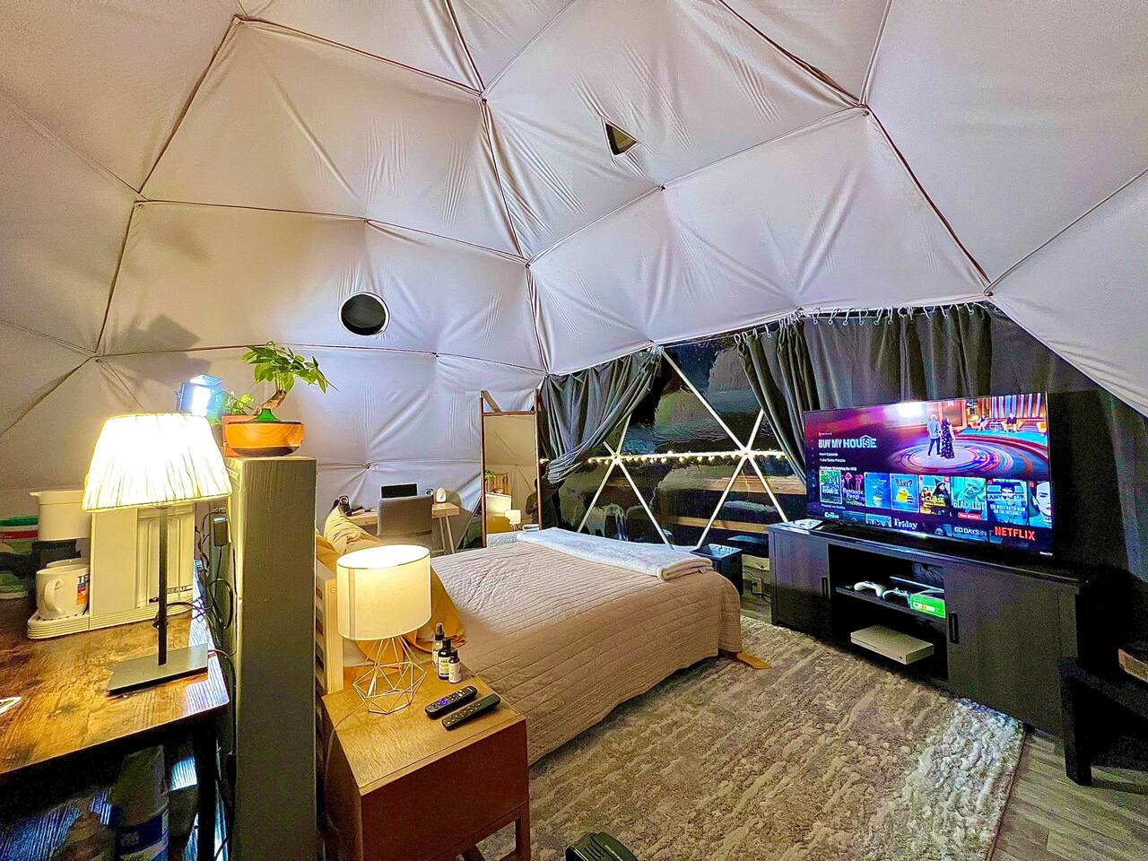 interior of a geodesic dome with a view of the bed, tv and window during the night